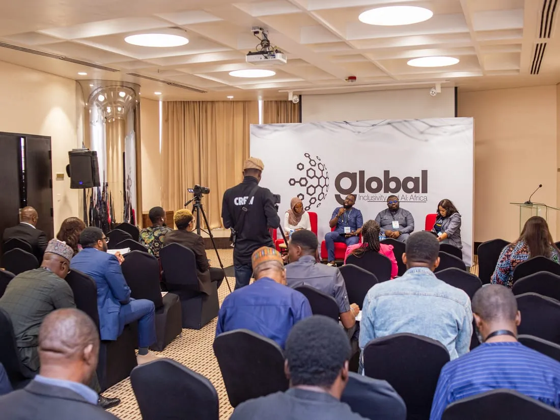 A panel session at a “Global Inclusivity and AI: Africa” event, with four speakers seated on stage in front of the event backdrop and an audience seated facing them.